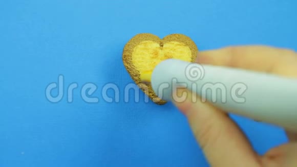 女性的手在蓝色背景上的心形饼干上画出有趣的表情符号并从管子上涂上棕色的糖霜视频的预览图