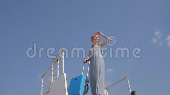带着旅行袋的年轻女子站在背景蓝天上的可移动楼梯上视频的预览图