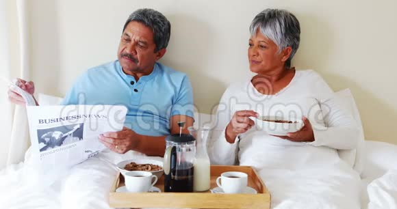 高年级夫妇在卧室4k吃早餐时看报纸视频的预览图
