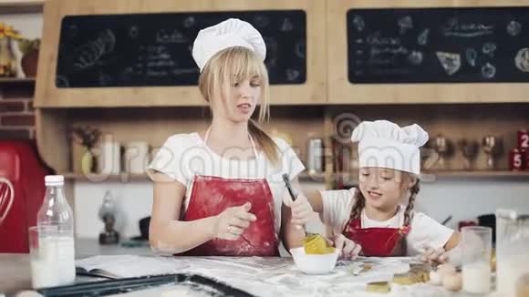 妈妈和女儿穿着同样的衣服在舒适的厨房里准备面团玩得很开心他们把鸡蛋放在碗里视频的预览图