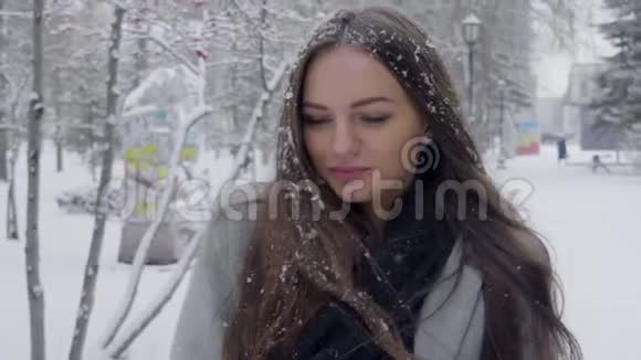在雪地背景下的冬季公园里一位时尚的年轻美女在户外的肖像雪落在她的头发上视频的预览图
