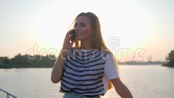 日落时分河堤上微笑女子的电话交谈视频的预览图