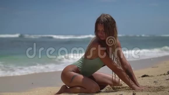 漂亮的模特长着一头金色长发双膝坐在柔软的沙滩上双手拉着沙子享受着视频的预览图