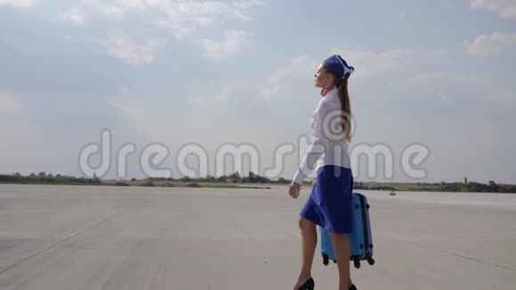 女乘务员穿着高跟鞋和制服带着手提箱沿着机场行驶视频的预览图