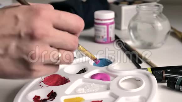 女性用手在调色板上用粉红色的颜料将画笔浸入然后与白色混合视频的预览图