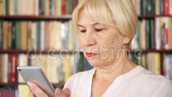 现代高级女性在家使用手机浏览阅读背景书架视频的预览图