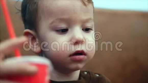 一个微笑的男孩坐在他母亲旁边通过瓶子里的红色吸管喝牛奶慢动作视频的预览图
