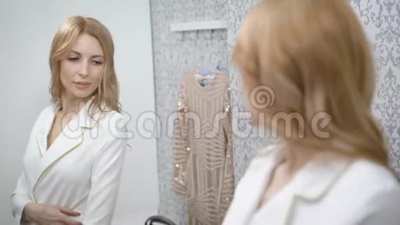 一位成年女性正在商场的更衣室里试穿白色时髦夹克照镜子视频的预览图