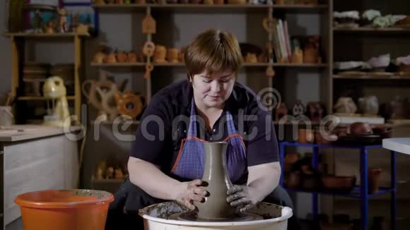 一位留着红色短发的成年妇女正在一个陶器车间里制作陶瓷花瓶在转盘上拉着粘土旋转视频的预览图