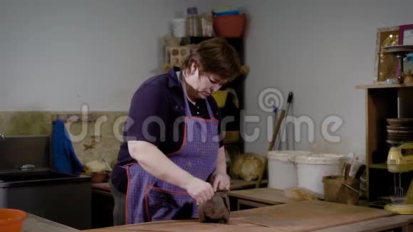 一位穿着围裙的成年妇女正在一家陶艺工作室的工作桌上用线切割一块粘土视频的预览图