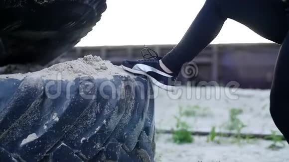 特写镜头女人双腿穿着黑白运动鞋跳上一个装满沙子的大型拖拉机车轮女运动员表演视频的预览图