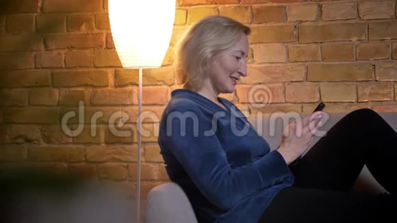 用电话和室内微笑拍摄白种人年长女性的特写镜头视频的预览图