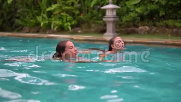 两个迷人的成年女孩正在私人住宅后院的游泳池里游泳她们游到泳池边视频的预览图