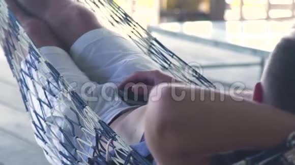 年轻人在夏季露台上的吊床上休息在暑假放松的时候男人在吊床上摇摆视频的预览图