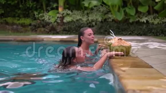 两个漂亮的朋友从美妙的私人游泳池的水中出来游泳池里有椰子鸡尾酒视频的预览图