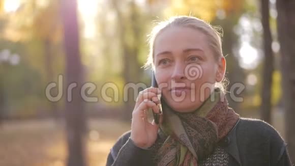 站在美丽的秋天公园里打电话的女人视频的预览图