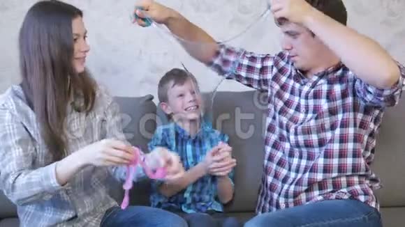 快乐的家庭妈妈儿子和爸爸玩泥浆坐在沙发上把黏液拉出来仔细看着视频的预览图