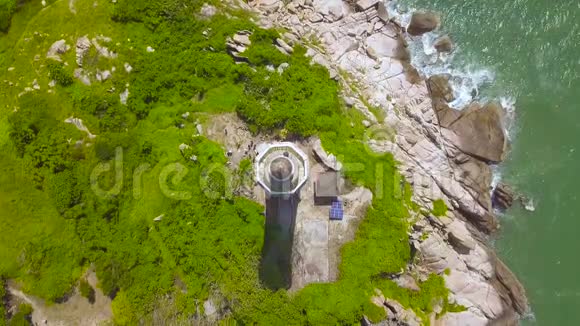 在蓝色的海洋里的岩石岛上的海景灯塔海洋绿色海岸的空中景观灯屋视频的预览图