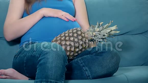 孕妇抚摸大肚子抱着菠萝香蕉水果坐在沙发上视频的预览图