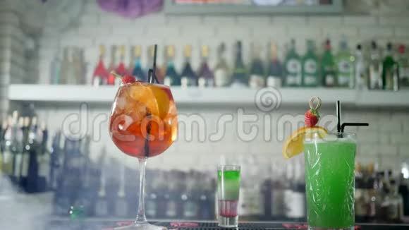 在酒吧内部背景下的烟雾中桌上摆着带有水果和塑料吸管的生动鸡尾酒视频的预览图