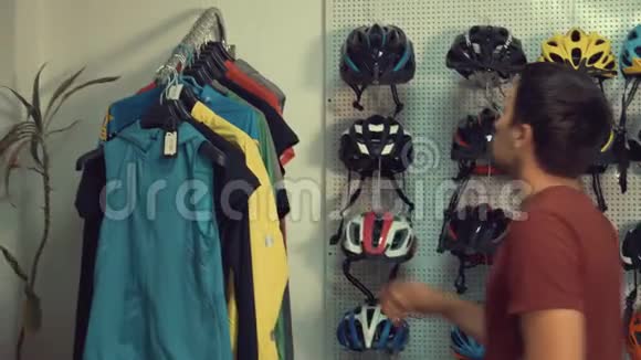 一个年轻的白人男子站在自行车商店的衣架上一架运动自行车衣服选择一个视频的预览图