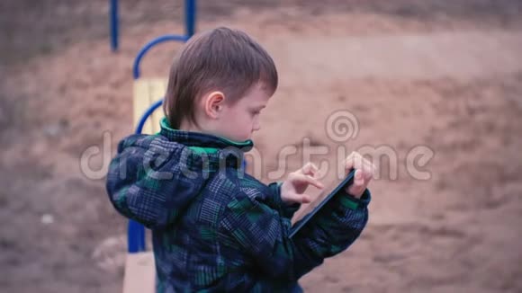 男孩摸着坐在公园里的长凳上的平板电脑屏幕侧视视频的预览图