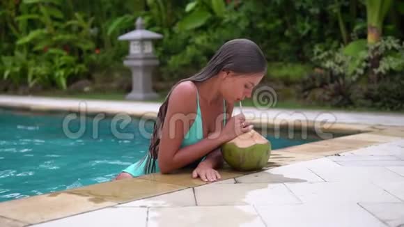 游泳运动员浑身湿透身材苗条手肘撑在游泳池边喝着椰子鸡尾酒视频的预览图