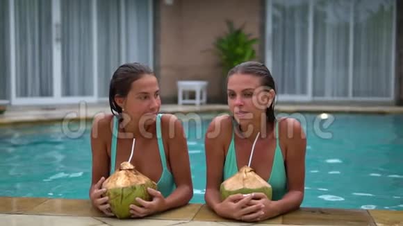 两个模特穿着比基尼在泳池边上用吸管喝椰子鸡尾酒女孩们玩得很开心视频的预览图