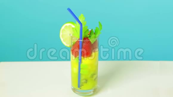 在一杯猕猴桃苹果和草莓切片中加入蓝色稻草装饰的水果鸡尾酒视频的预览图