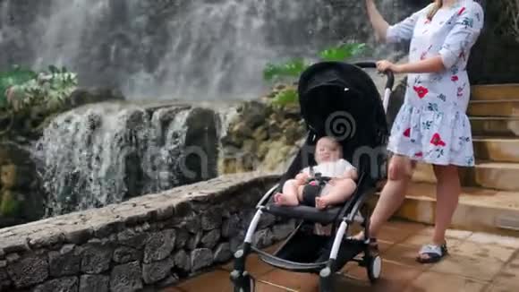 一位年轻的母亲带着她的孩子在瀑布附近散步在旅行时在智能手机上拍照视频的预览图