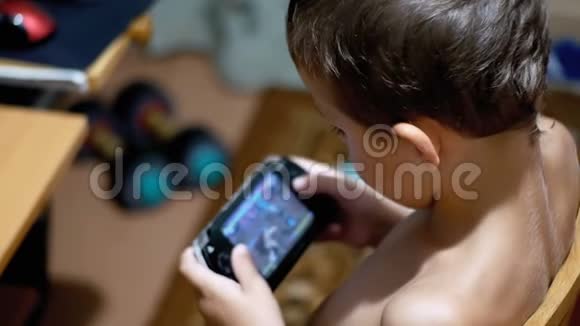 8岁的孩子坐在家里的椅子上在便携式游戏机上玩电子游戏视频的预览图