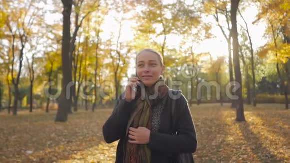 站在美丽的秋天公园里打电话的女人视频的预览图