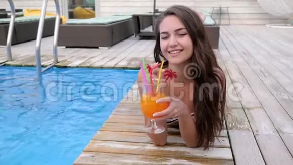 暑假期间可爱的女孩在游泳池附近喝着吸管酒精饮料视频的预览图