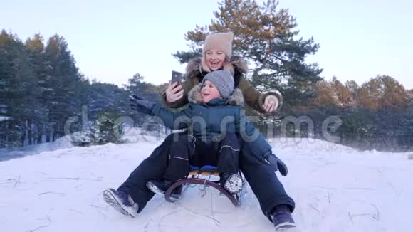 在雪山上雪橇上的妈妈和儿子用手机拍照视频的预览图