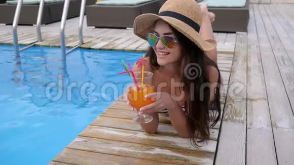 游泳池边有一个女孩度假时戴着帽子戴着墨镜手里拿着鸡尾酒的迷人女性的肖像视频的预览图