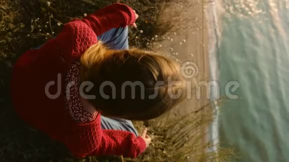年轻冷静的姜姑娘穿着红色毛衣在岩石海岸边眺望大海视频的预览图