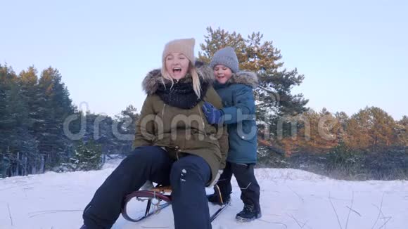 冬天的娱乐快乐的母子骑着雪橇在雪地里露天进入森林视频的预览图