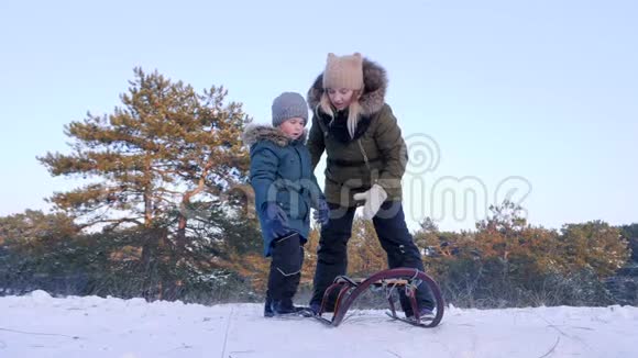 冬天森林里的家庭休息妈妈在新鲜空气的特写镜头里把快乐的小儿子推上雪橇视频的预览图