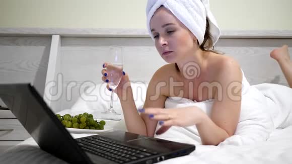 头上戴毛巾的女孩带着香槟在社交网络上交流在床上用笔记本电脑交流视频的预览图