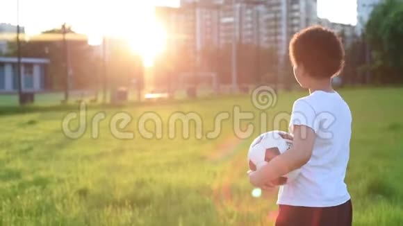 可爱的男孩在公园的夕阳下用足球踢足球s视频的预览图