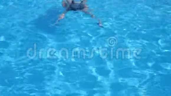 女游泳者在游泳池里漂在纯蓝色的水里视频的预览图