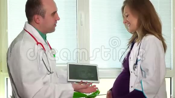 男医生和孕妇同事在平板电脑上显示超声波照片视频的预览图