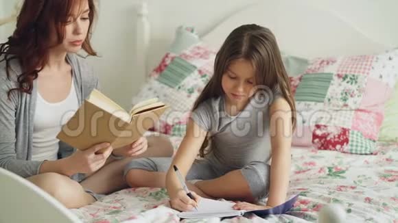 细心的妈妈帮她可爱的小女儿做小学作业爱妈妈看书爱女孩视频的预览图