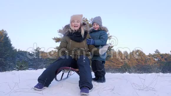 冬季的户外乐趣母亲和儿子乘雪橇缓慢地进入森林视频的预览图