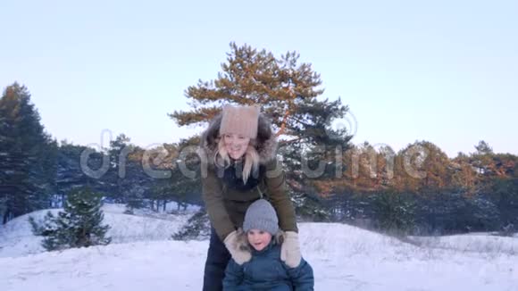 冬天快乐的年轻女子把儿子从雪山上推着雪橇慢悠悠地追着他跑视频的预览图
