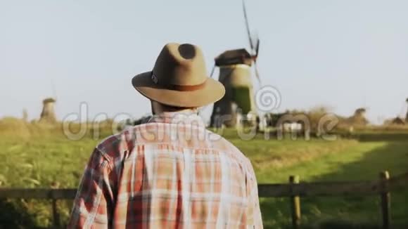 4K成功的高加索风车农民工人穿着伐木工衬衫和帽子的人在阳光明媚的绿色田野里四处张望视频的预览图