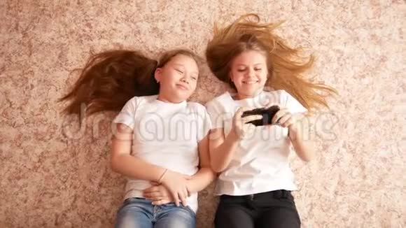 两个十几岁的女孩躺在地板上笑着拍手机头发散落在地板上视频的预览图