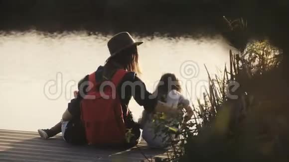 日落时分女人小女孩和男孩坐在码头上令人惊叹的电影镜头幸福团结统一观念4K视频的预览图