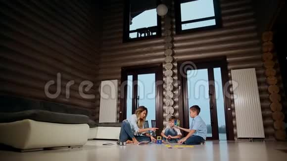 快乐的母亲带着两个孩子坐在乡间别墅的地板上花时间一起收集孩子视频的预览图