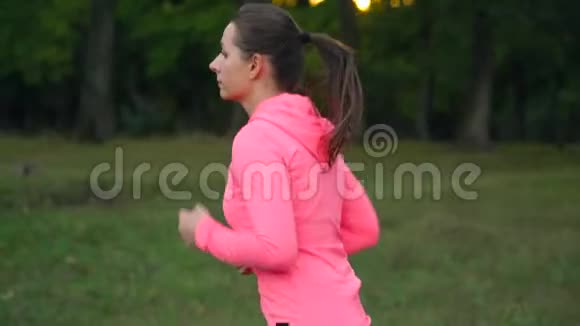 日落时分一个女人穿过一个秋天的公园向后看慢动作视频的预览图